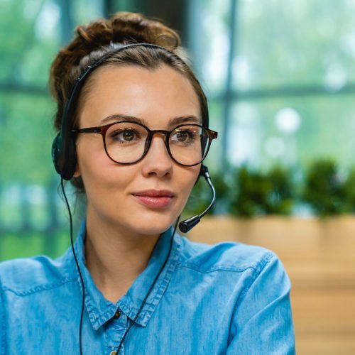 Side view shot of young successful businesswoman wearing glasses and headphones in office